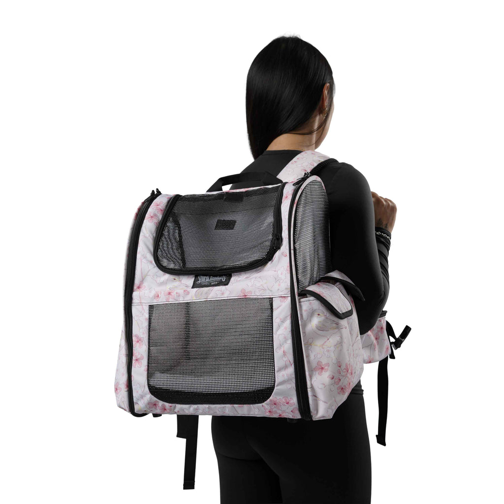 Woman wearing a white pet backpack with pink floral print, mesh panels, and side pockets.