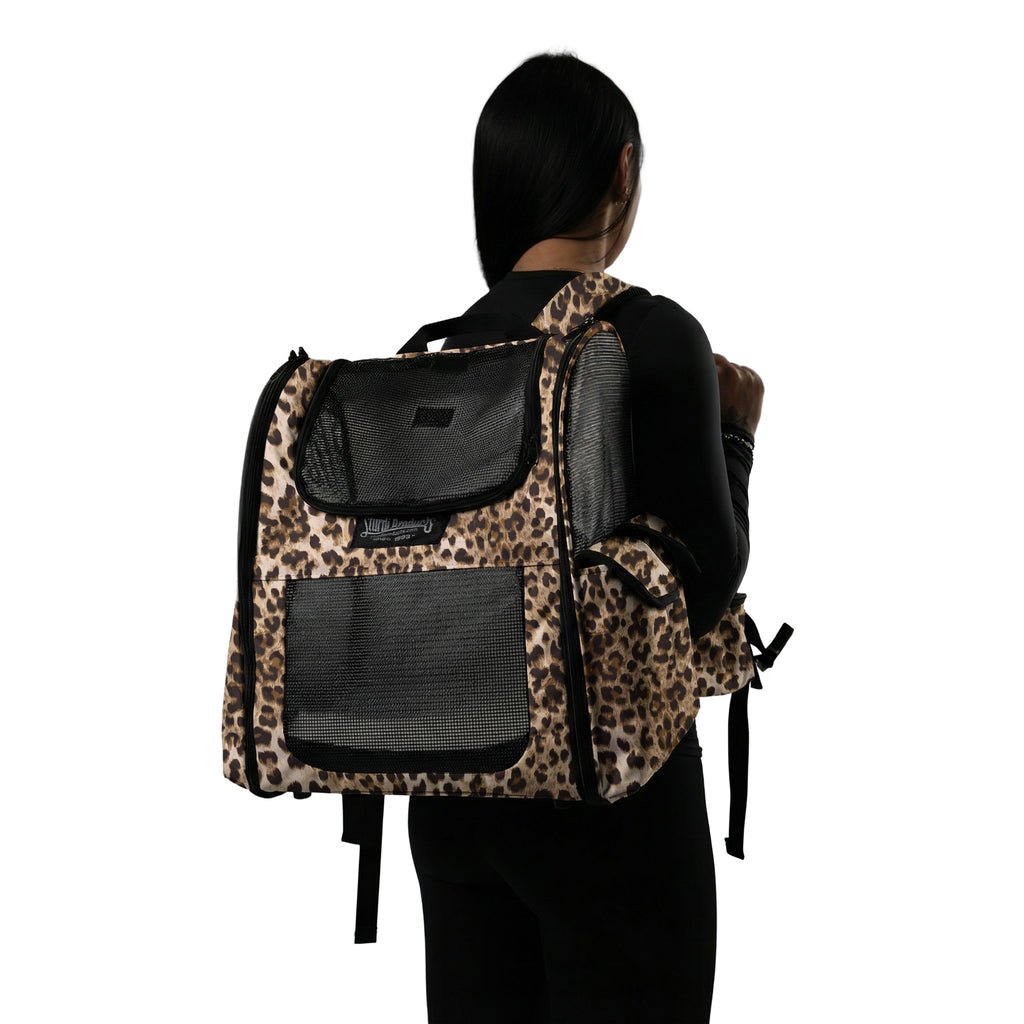 Woman wearing a leopard print pet backpack with mesh panels and storage pockets.