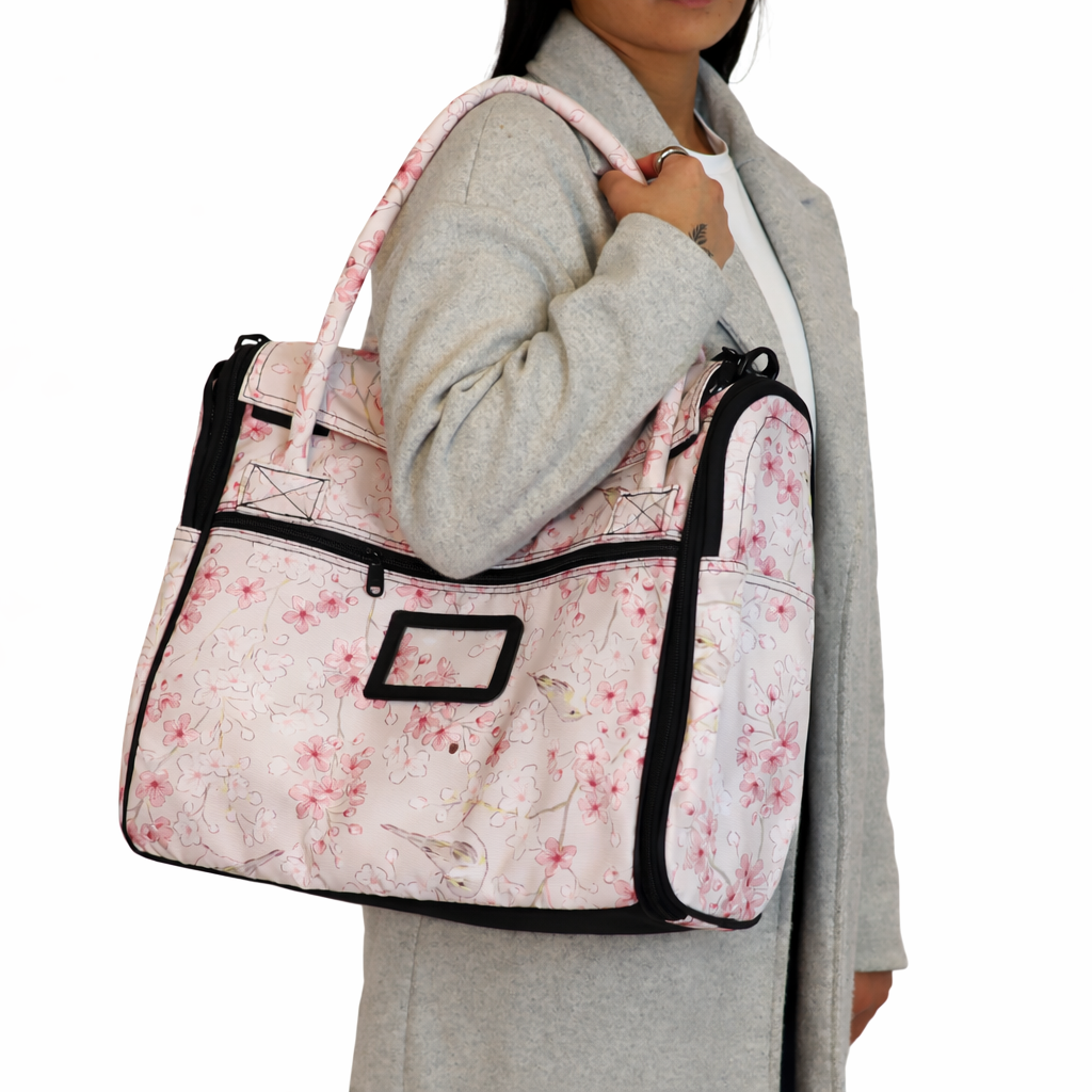 Woman carries a pink floral pet travel tote with black trim and multiple zippers over her shoulder.