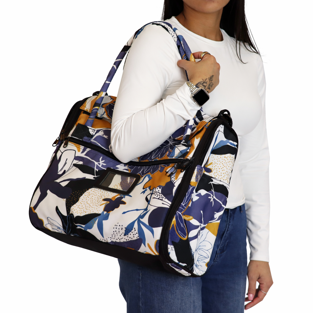 Woman carrying a stylish Incognito pet travel tote with a vibrant floral and abstract pattern in blues, gold, and white.