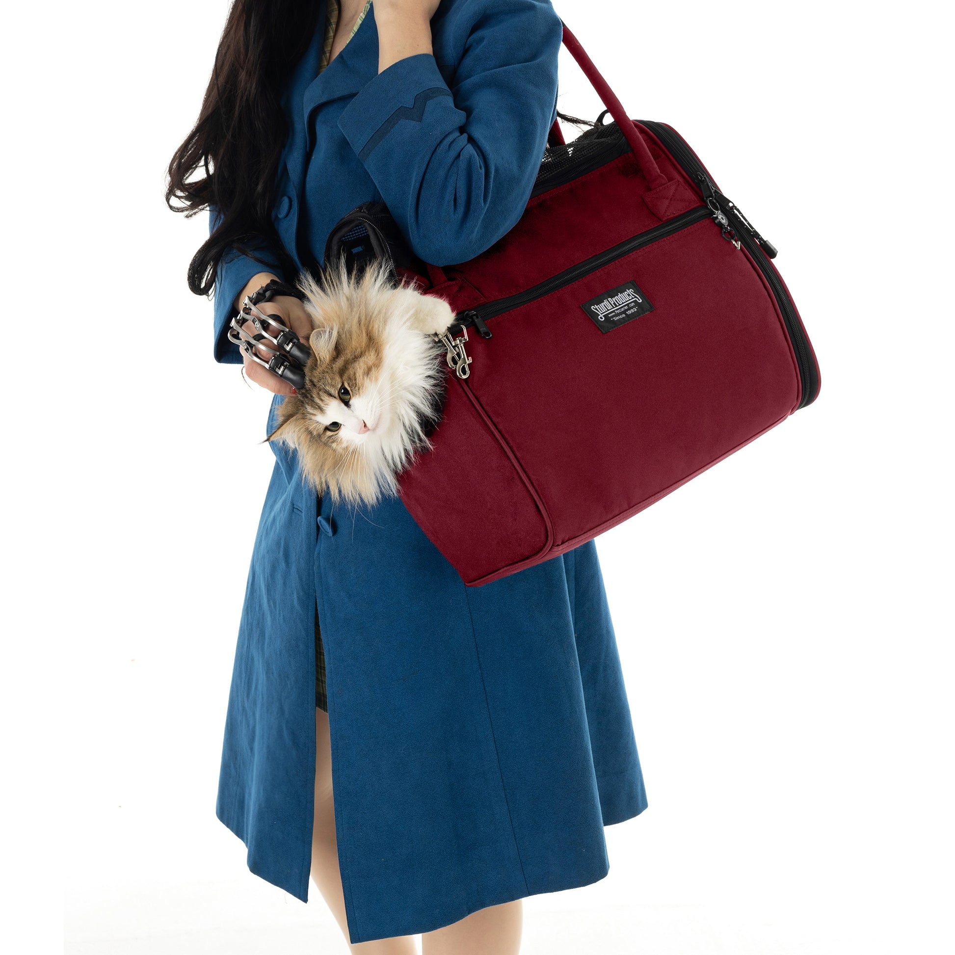 Woman in blue coat carrying a burgundy Incognito pet travel tote with a fluffy cat peeking out.