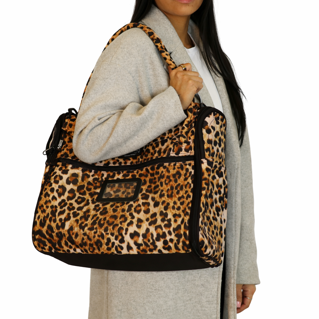 Woman carries a stylish Incognito leopard print pet travel tote with mesh windows and a shoulder strap.