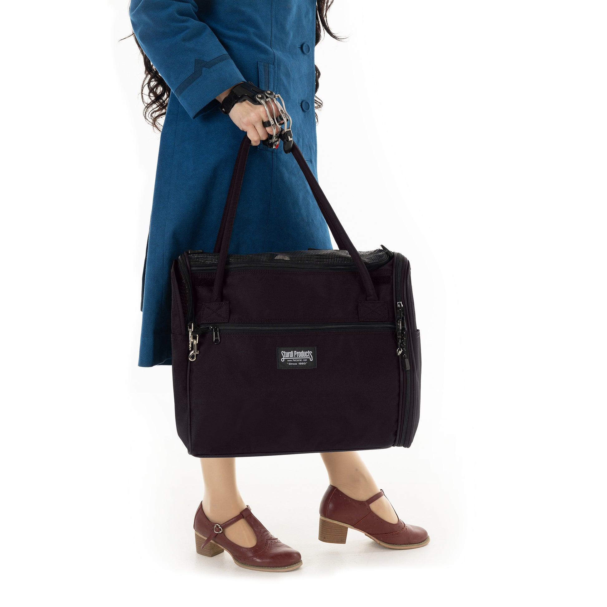 Person in blue coat holding a black Incognito discreet pet travel tote with mesh panels and zippers.