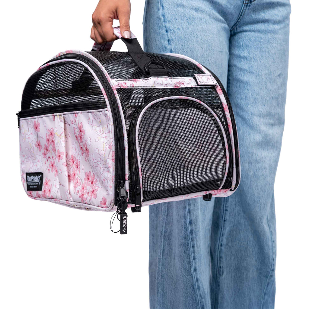 Person holding a pink floral pet carrier with black mesh panels and a top handle.
