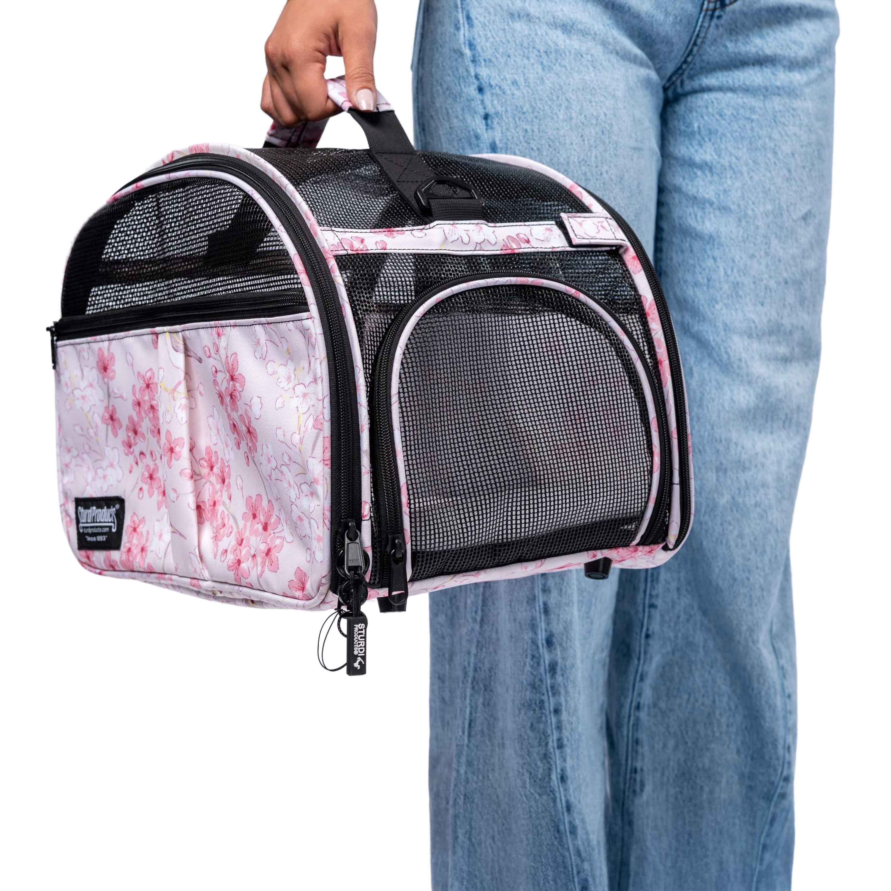 Person holding a pink floral pet carrier with black mesh panels and a top handle.