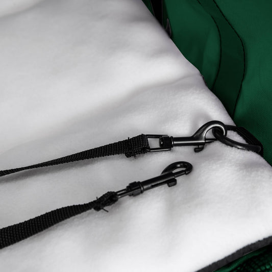 Black nylon safety tether with two metal clips on a white fleece lining inside a green pet carrier.