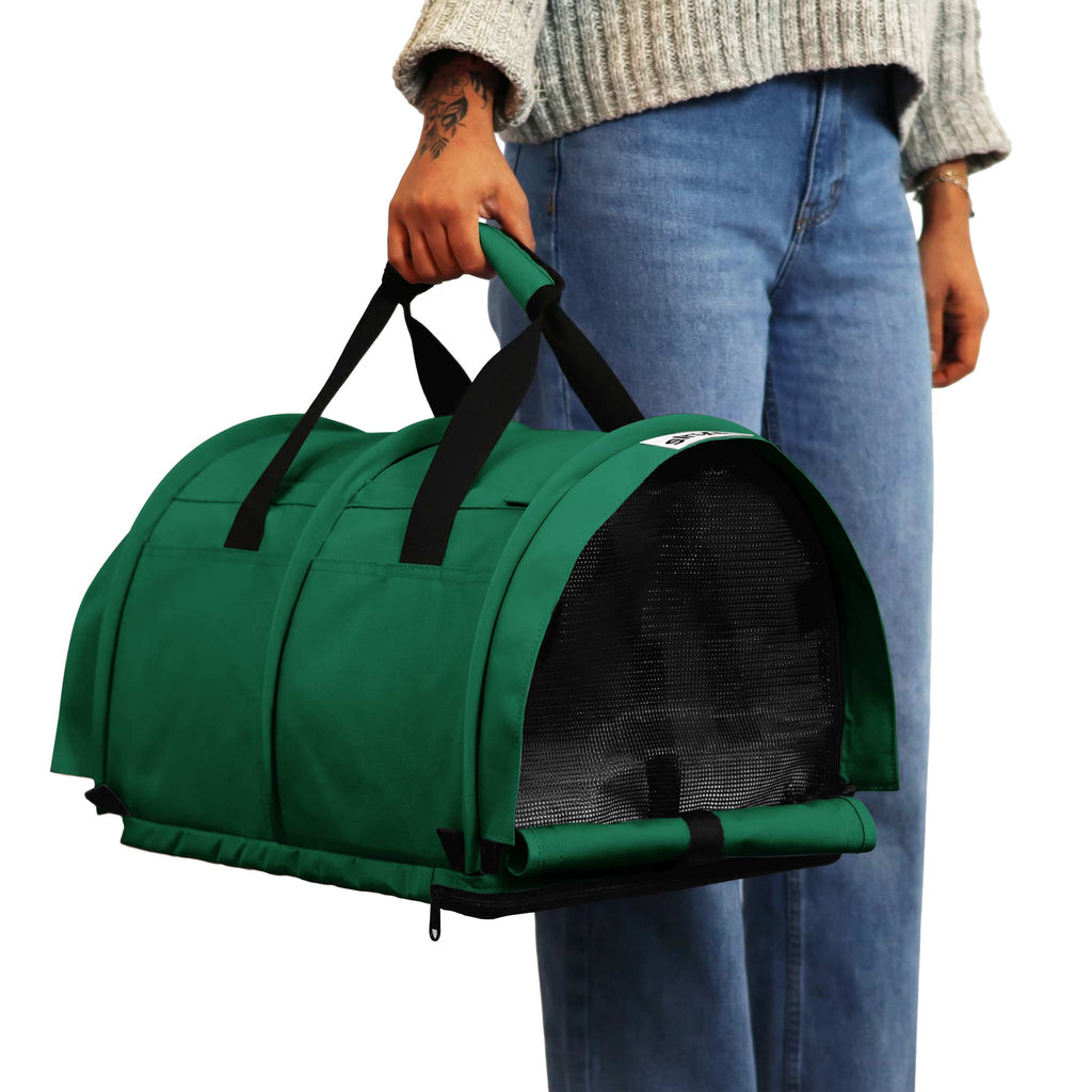 Person holding a green SturdiBag Pro 3.0 divided pet carrier with black mesh windows and handles.