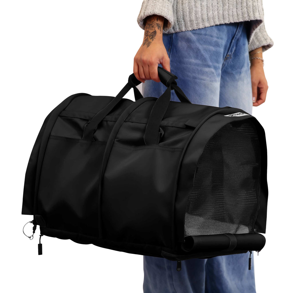 Person holding a black SturdiBag Pro 3.0 divided pet carrier with mesh panels and top handles.