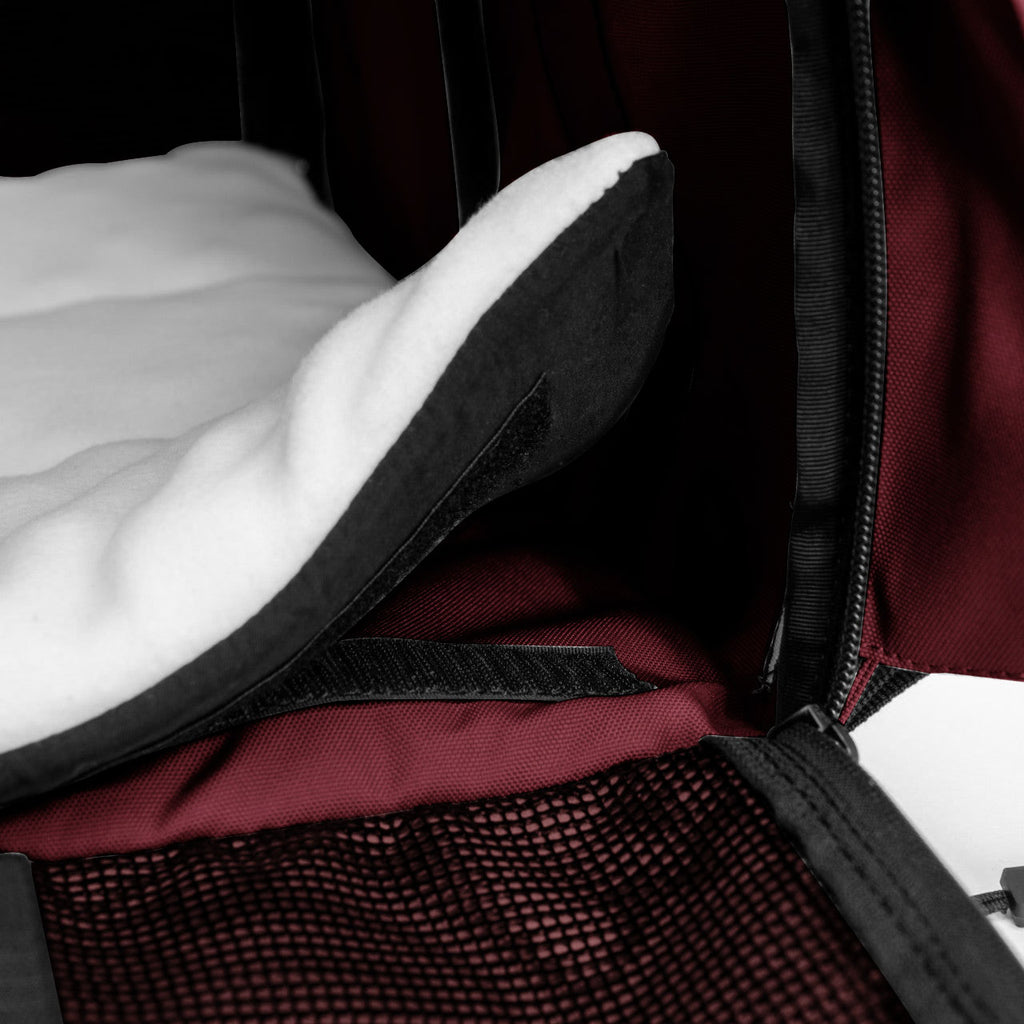 Close-up of a burgundy SturdiBag Pro 3.0 pet carrier interior with a white fleece pad and black mesh pocket.