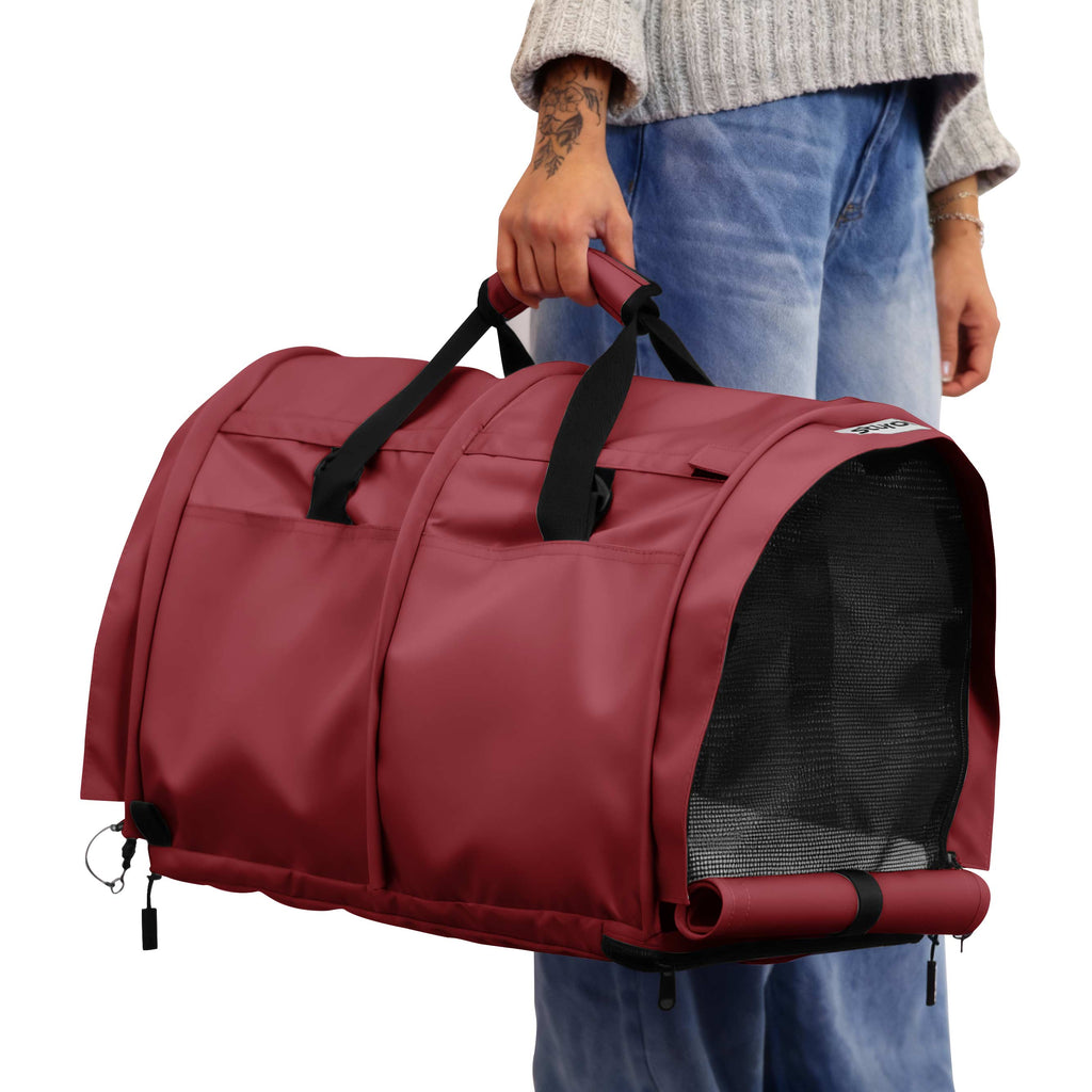 Person holding a red SturdiBag Pro 3.0 divided pet carrier with mesh panels and black straps.