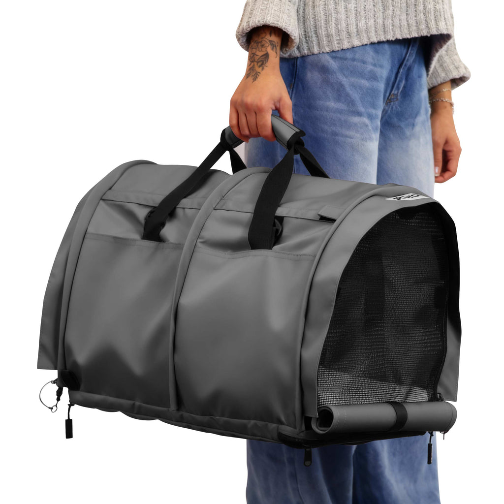 Person holding a gray SturdiBag Pro 3.0 divided pet carrier with mesh panels and black handles.