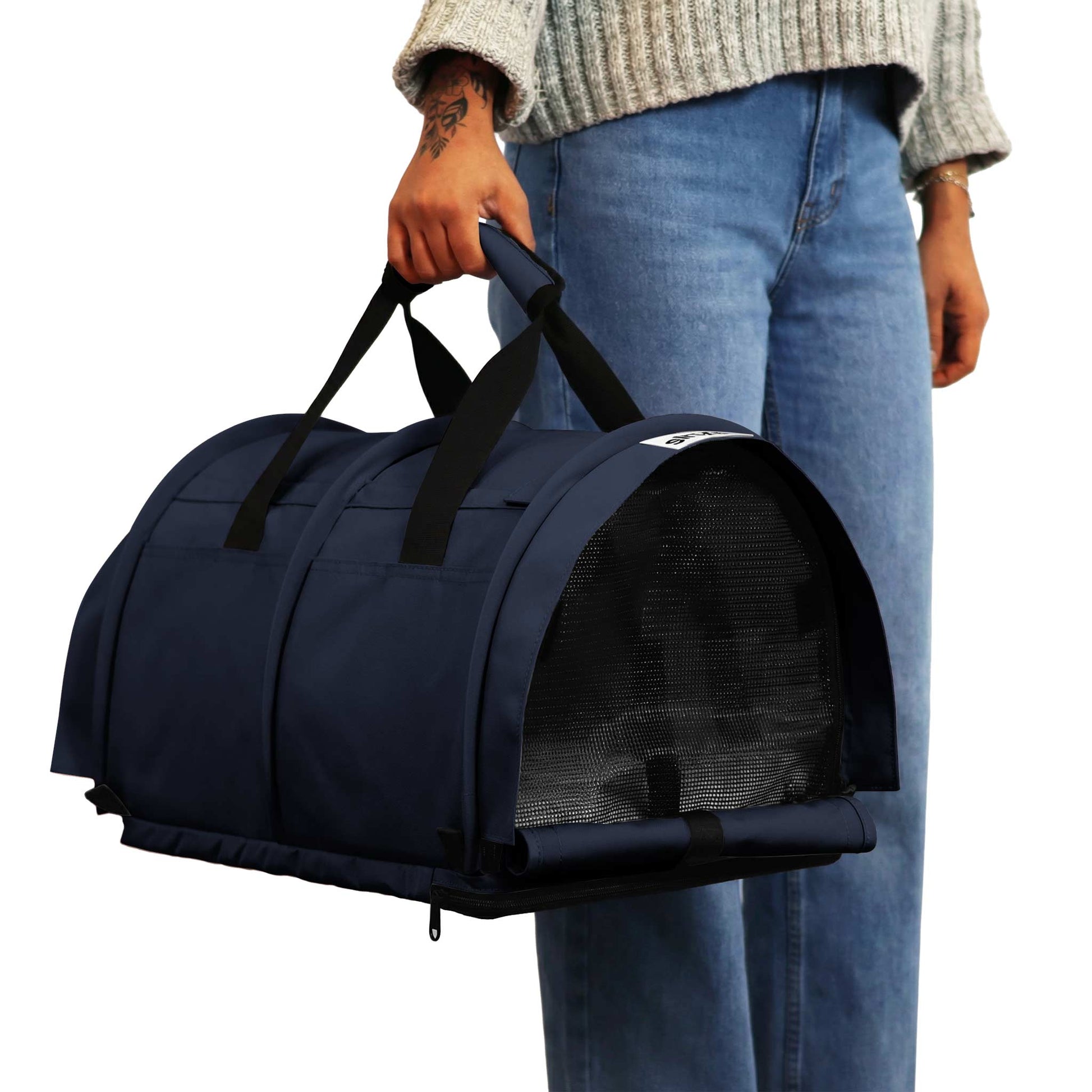 Person carrying a navy blue SturdiBag Pro 3.0 pet carrier with mesh window and black handles.