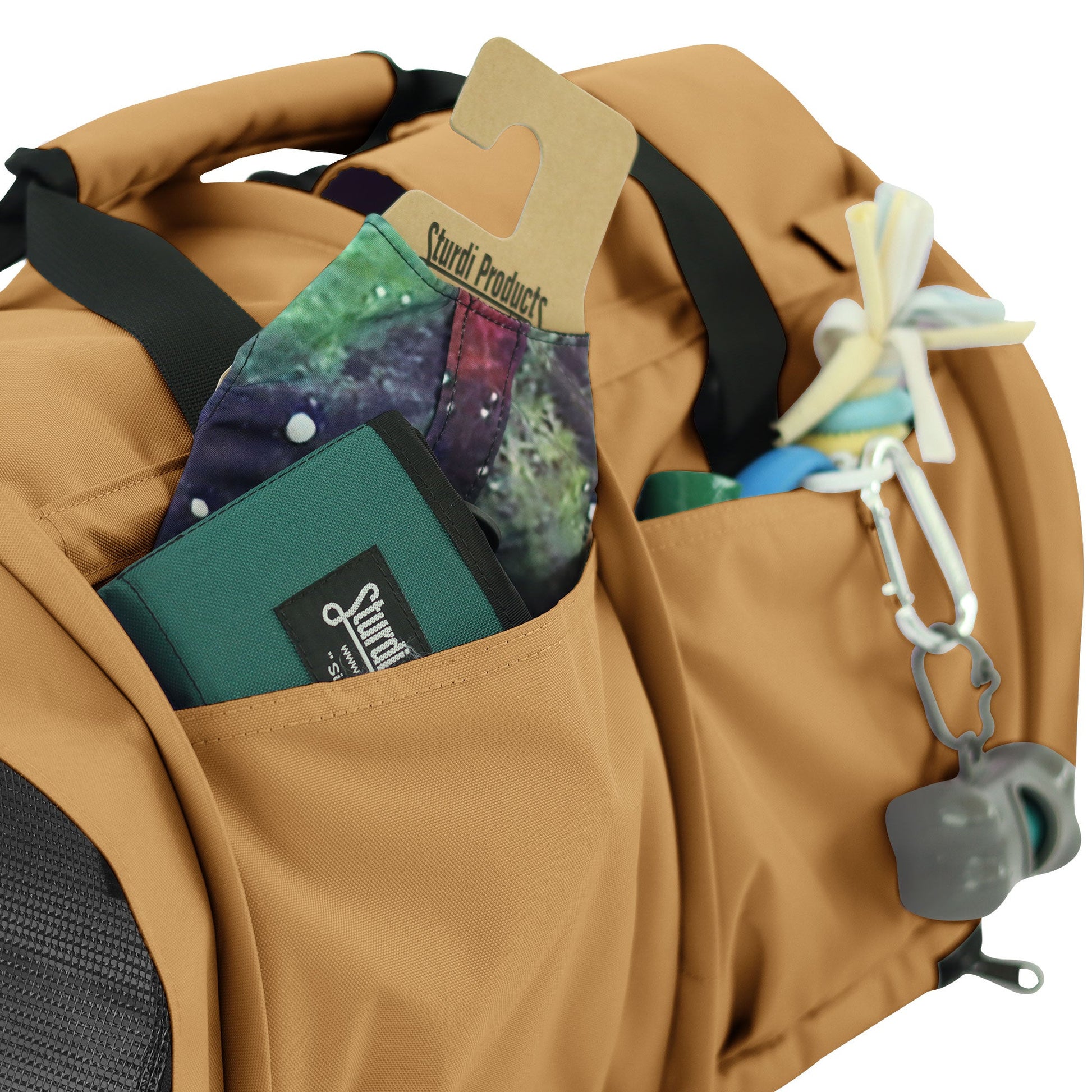 Tan SturdiBag Pro 3.0 pet carrier with side pockets holding a green wallet, colorful fabric, and pet accessories.