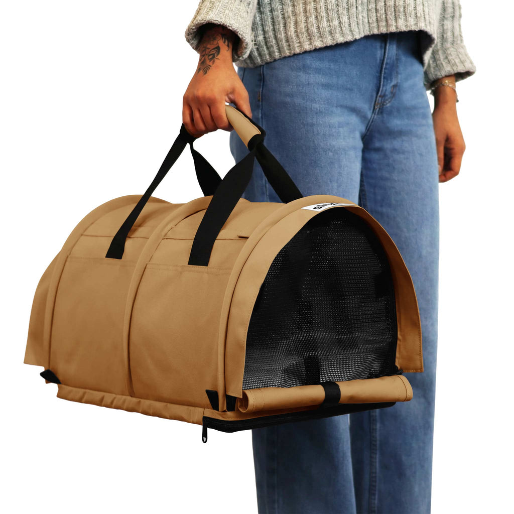 Person holding a tan SturdiBag Pro 3.0 pet carrier with black mesh and straps.