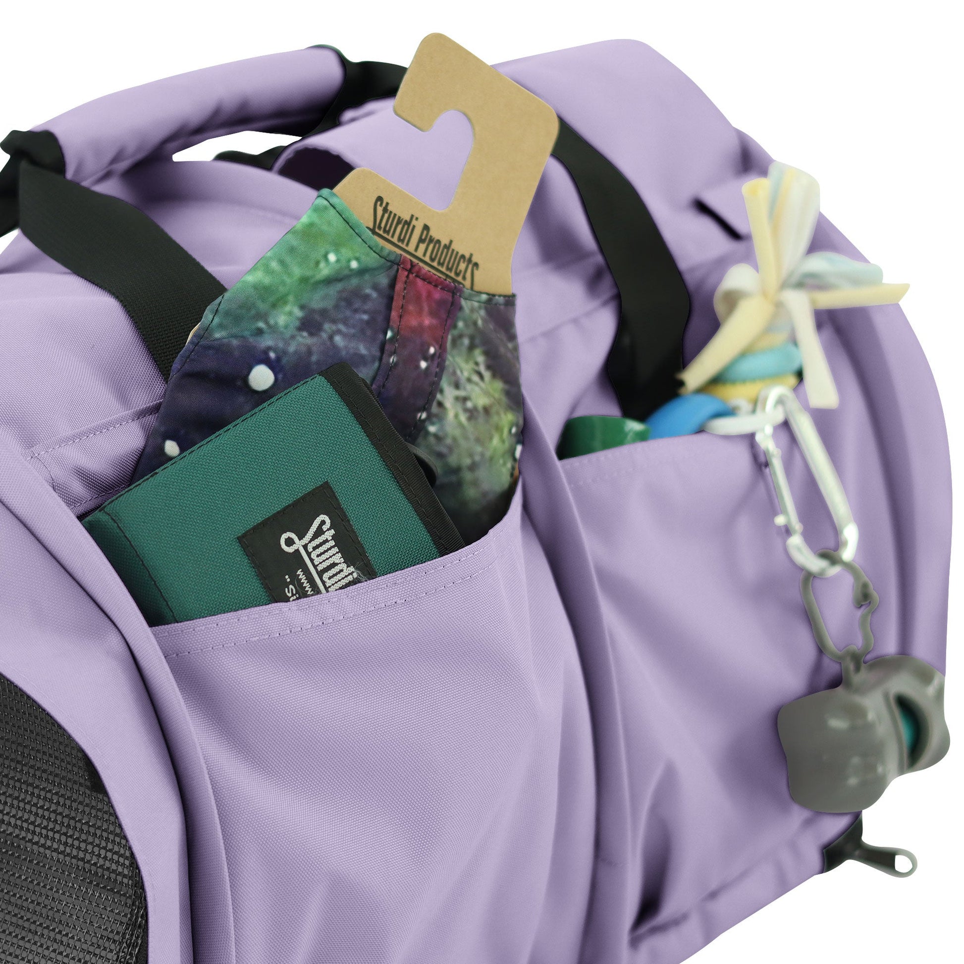Lavender SturdiBag Pro 3.0 pet carrier with side pockets holding a wallet, fabric, and pet toys.