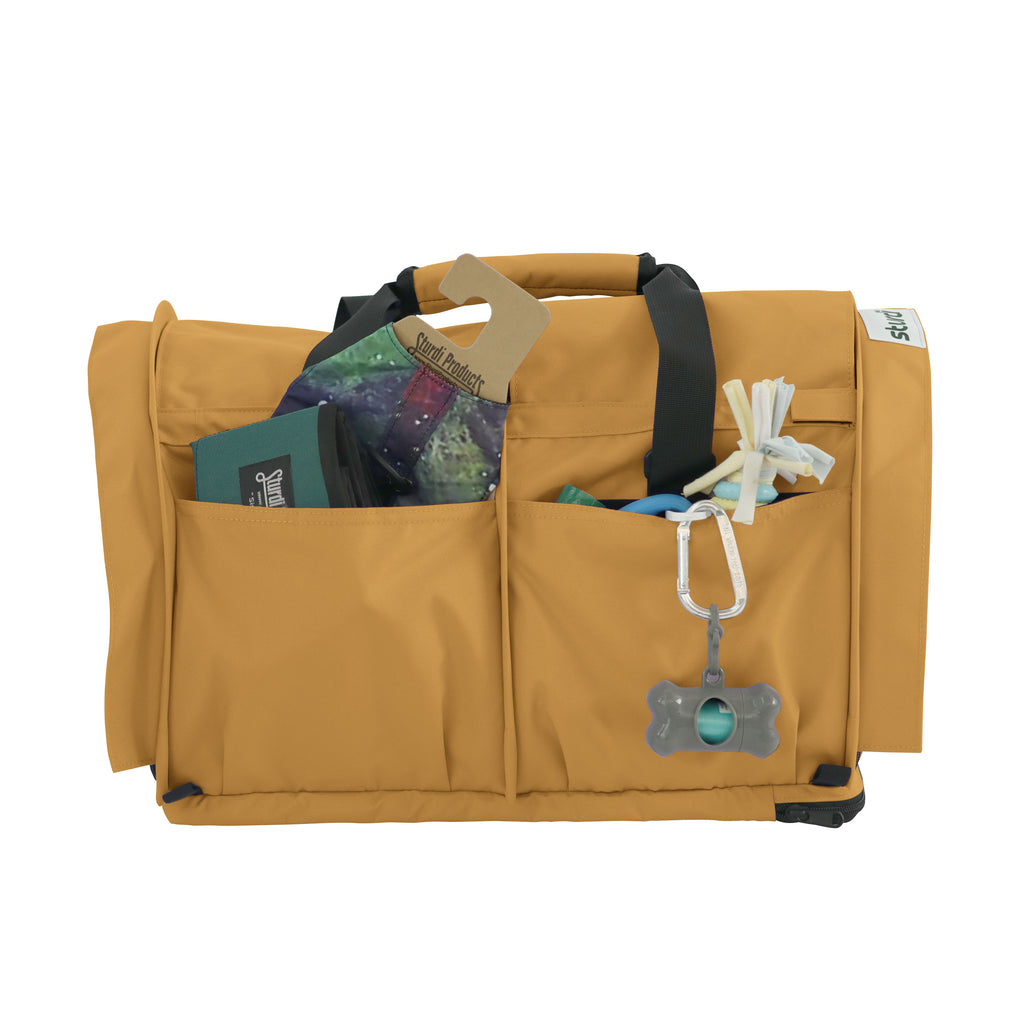 Tan SturdiBag Pro 3.0 pet carrier with front pockets holding pet essentials and a carabiner.