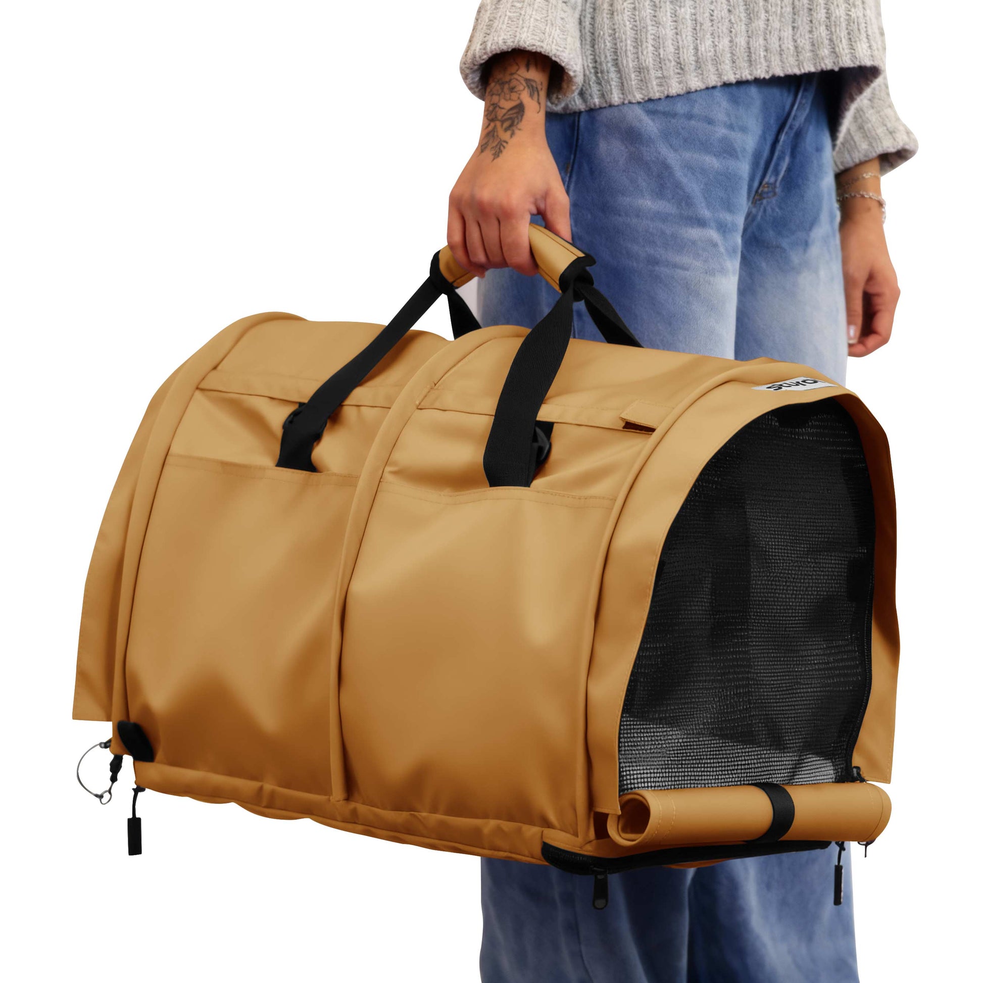 Tan SturdiBag Pro 3.0 soft-sided pet carrier with black mesh window and handles, held by a person.