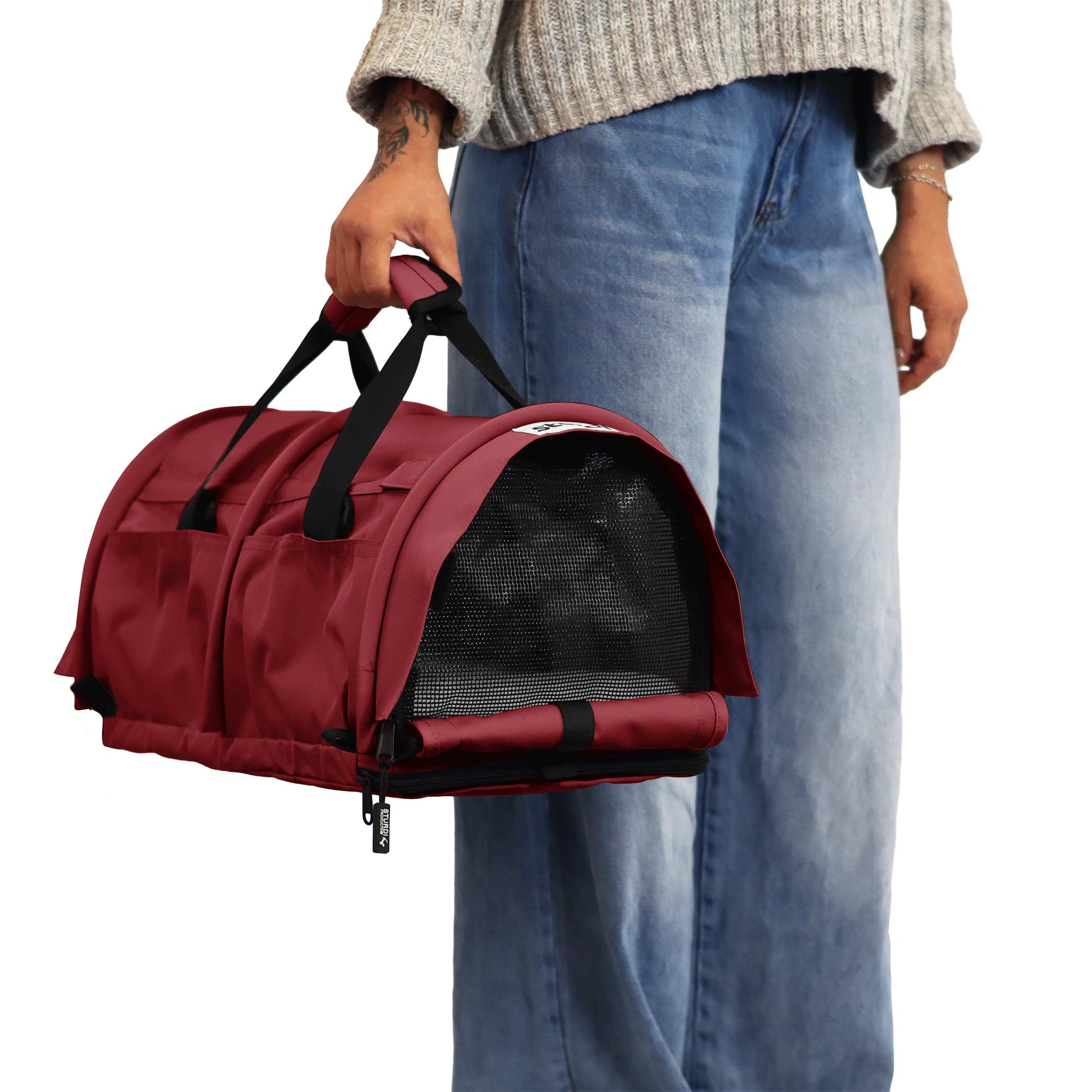 Person holding a red SturdiBag Pro 3.0 soft-sided pet carrier with mesh window and black straps.