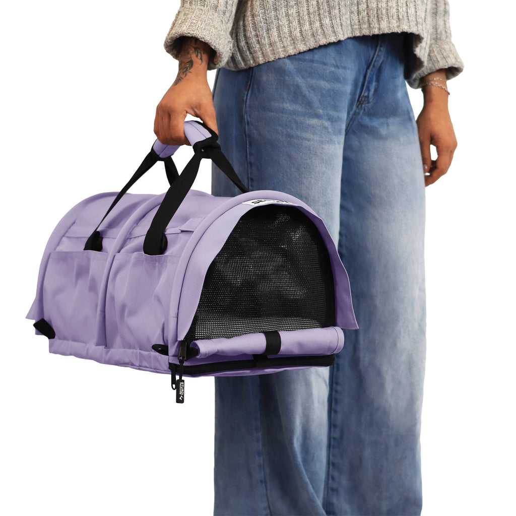 Person holding a lavender SturdiBag Pro 3.0 soft-sided pet carrier with mesh window and black straps.