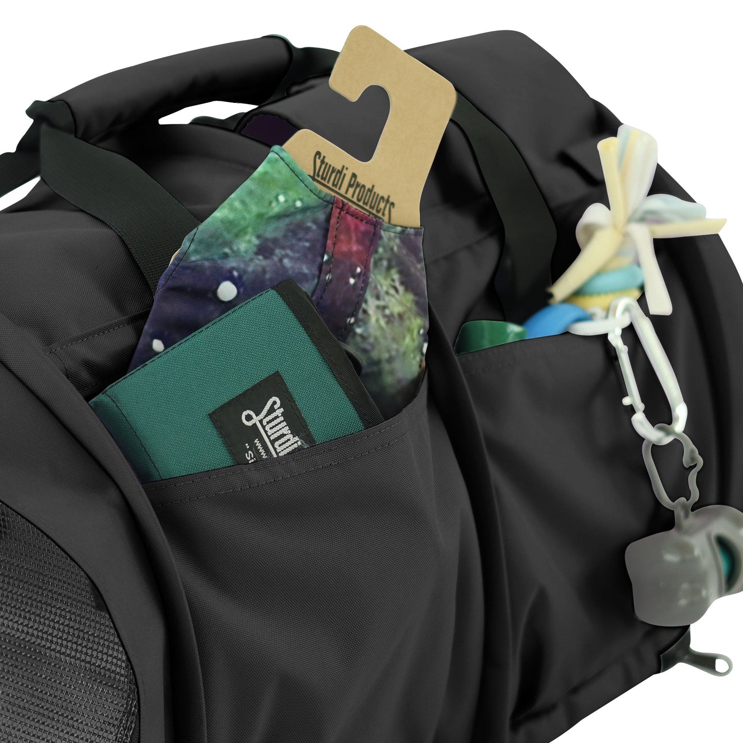 Black SturdiBag Pro 3.0 pet carrier with side pockets holding a green wallet, colorful fabric, and pet toys.