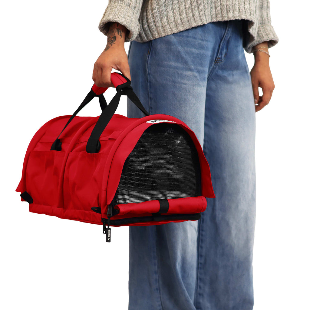 Person holding a red SturdiBag Pro 3.0 soft-sided pet carrier with black mesh windows and handles.
