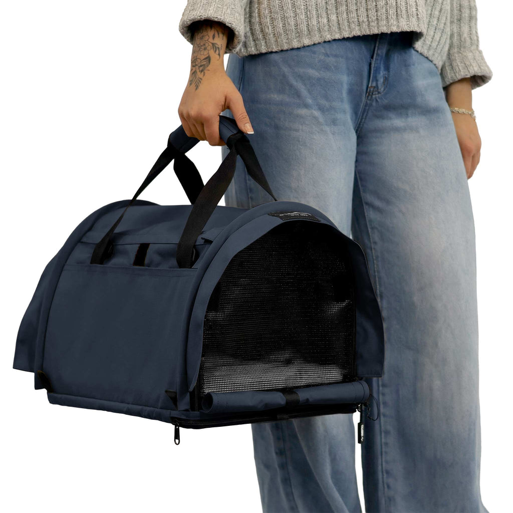 Person holding a navy blue SturdiBag Pro 3.0 soft-sided pet carrier with mesh window.