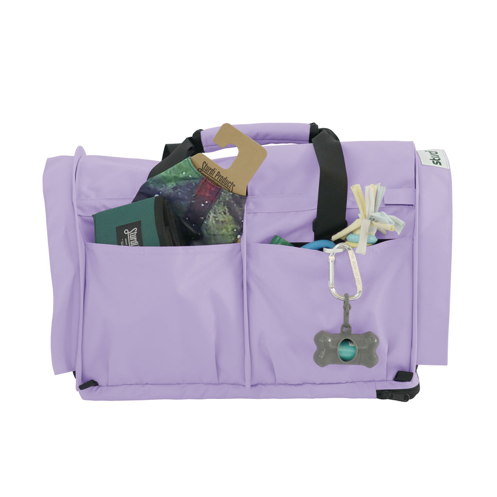 Lavender SturdiBag Pro 3.0 pet carrier with black straps, mesh panels, and front pockets holding pet essentials.