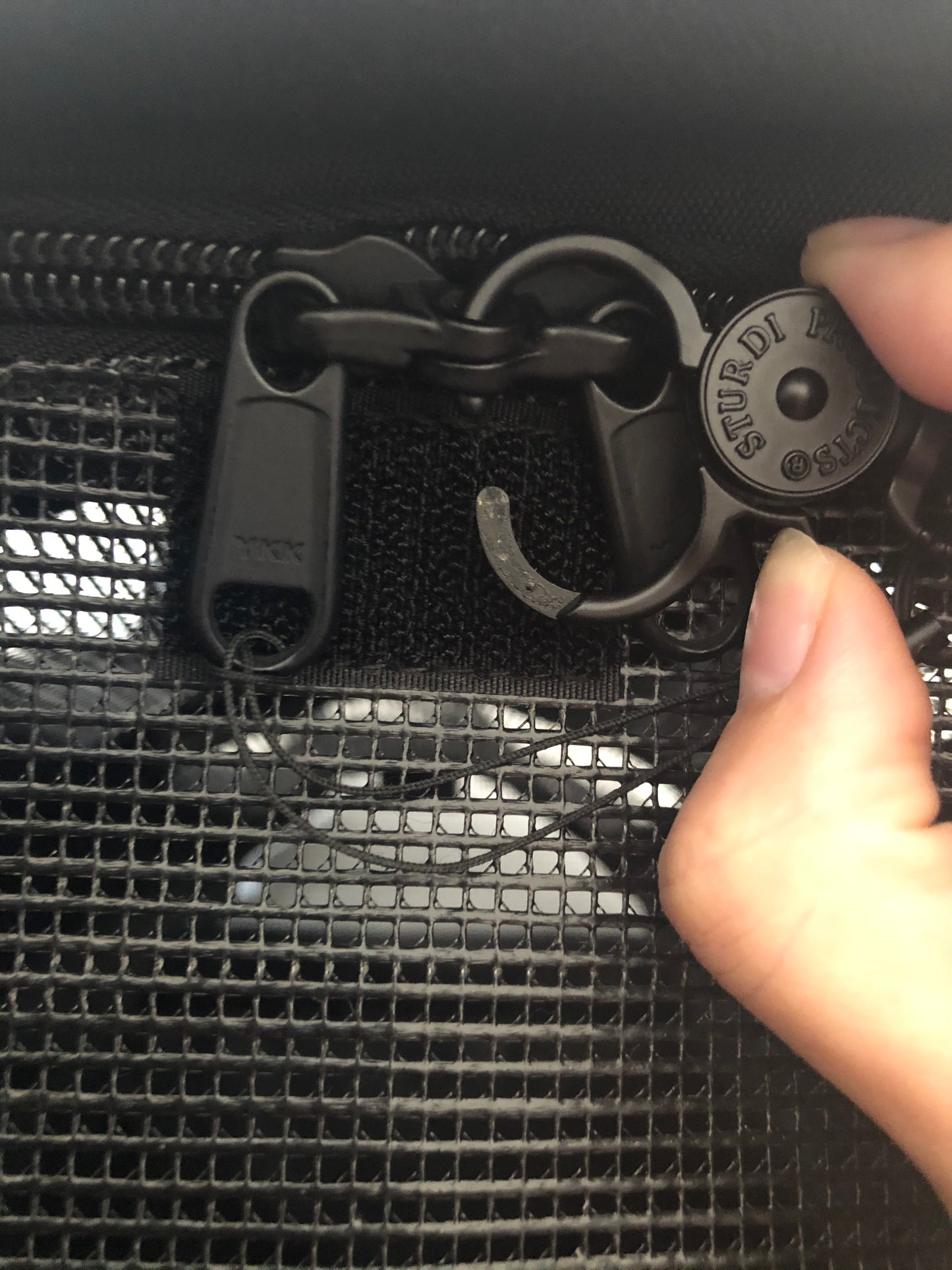 Black Sturdi Products zipper safety clip securing two zipper pulls on a pet carrier's mesh panel.